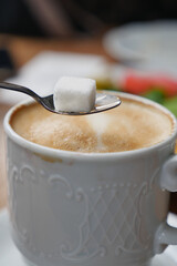 Coffee with sugar cube on spoon at cozy cafe table