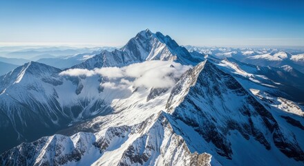 Obraz premium Aerial view of snow covered mountain range under a clear blue sky with some clouds around the peaks
