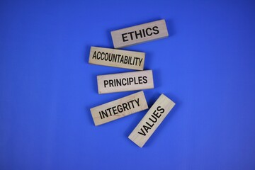 Wooden blocks stacked with words representing ethics, values, accountability, and principles, set against a blue background symbolizing morals and foundational virtues.