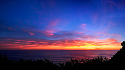 Obraz premium Stunning sunset over the ocean with vibrant colors and silhouetted foreground vegetation