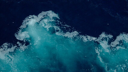 Open sea with deep blue water and white foamy waves left by a moving ship