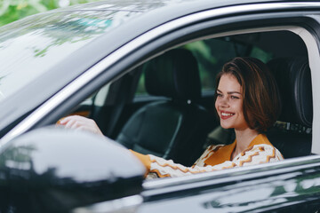 Naklejka premium A smiling woman sits behind the wheel of a sleek car, enjoying a sunny drive and a relaxed moment in the interior.