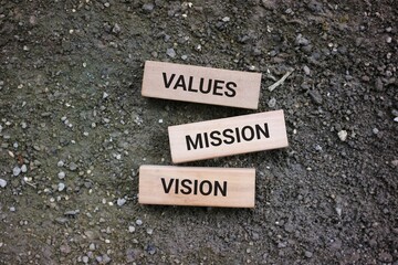 Wooden cubes labeled with values, mission, and vision, symbolizing foundational principles for organizations and individuals. The rough ground background