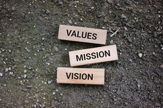 Wooden cubes labeled with values, mission, and vision, symbolizing foundational principles for organizations and individuals. The rough ground background