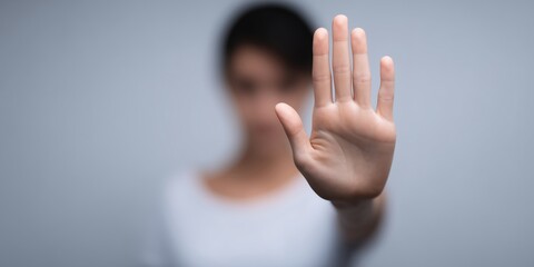 Woman with raised hand in foreground, signaling stop, blurred background creating a sense of urgency and focus on the gesture, conveying a message of caution and awareness
