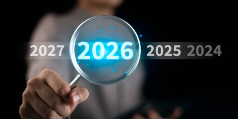 Businessman holding magnifying glass focusing on 2026 among years, symbolizing future forecast, business vision, strategic planning, financial prediction, growth opportunities upcoming trends.