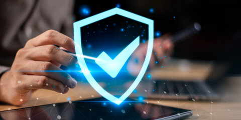 Hand touching tablet with glowing shield and check mark, symbolizing cybersecurity, data...