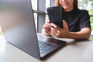 Closeup image of a woman using smart phone and laptop computer in cafe