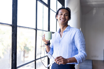 Business professional holding coffee cup, smiling by office window, enjoying break