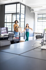 Colleagues carrying box and smiling while moving into modern office space