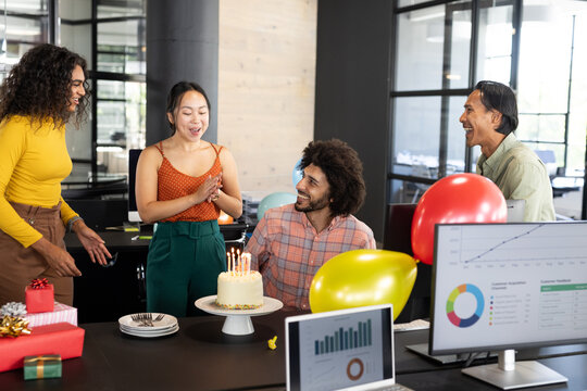 In office, celebrating birthday with cake and balloons, diverse colleagues gathering