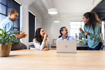 Diverse team collaborating and sharing ideas around laptop in modern office