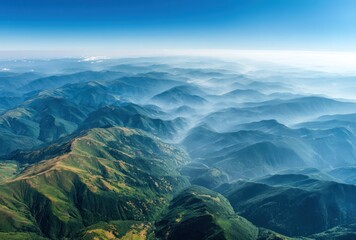Aerial view shows ranges of blue & green mountains fading into a misty horizon, under a bright blue sky on a clear sunny day