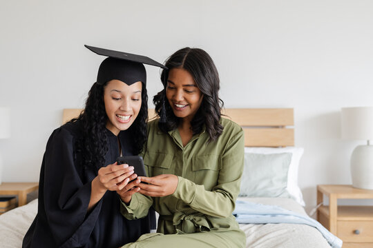 Graduate in cap and gown sharing joyful moment with friend on smartphone