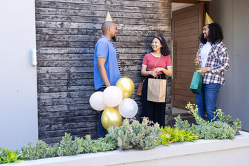 Friends celebrating with balloons and gifts, smiling and chatting at front porch