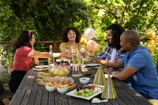 Toasting with wine glasses, friends celebrating and sharing festive meal outdoors