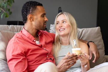 Couple sitting on couch enjoying cupcakes, sharing joyful conversation at home