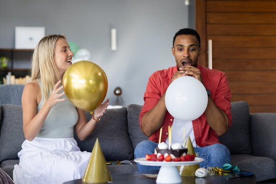 Friends inflating balloons on couch, preparing for festive celebration at home