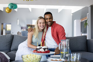 Happy couple celebrating birthday at home with cake and balloons, smiling joyfully