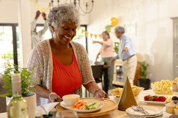 Elderly woman serving snacks at family gathering, smiling and enjoying celebration
