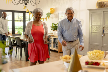Elderly couple joyfully dancing at home during festive celebration with friends © wavebreak3