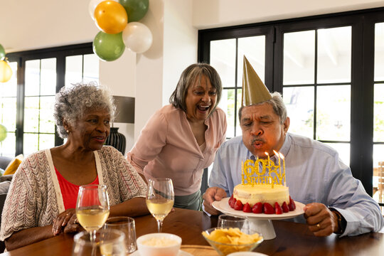 Elderly man blowing out birthday candles while friends celebrate with joy
