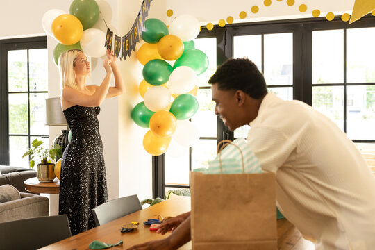 Decorating for party, woman hanging banner while man arranges table decorations - Powered by Adobe