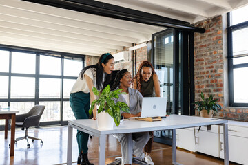 In office, colleagues sharing ideas enthusiastically while collaborating around laptop