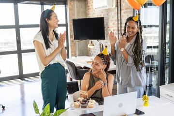 Celebrating birthday, colleagues in office clapping with cupcakes and party hats