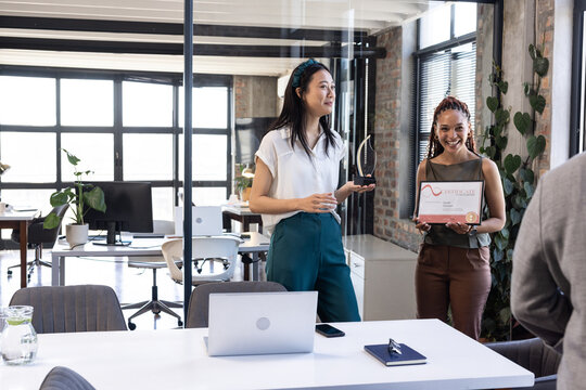Celebrating achievement in office, woman holding certificate with smiling colleagues
