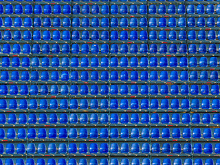 Rows of empty blue stadium seats creating a geometric pattern in an outdoor sports arena.