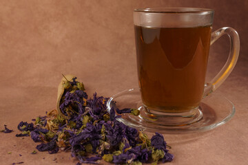 Glass cup of herbal tea with dried mallow flowers and wooden spoon on brown background promoting...