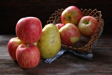 Ripe red apples in a basket with a ripe pear on a wooden table