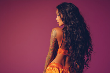 Stylish woman with flowing dark hair poses against a vibrant purple background showcasing her colorful tattoos and confident demeanor