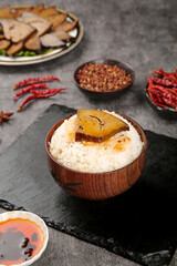 Asian braised pork belly rice bowl with spicy chili peppers and traditional side dishes on slate table