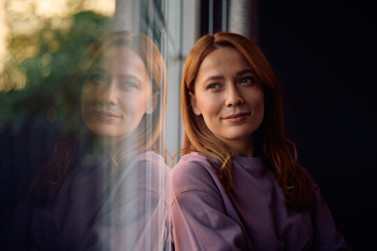 Smiling woman day dreaming while leaning on window.