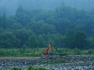 夏の大雨の日の川と森の風景と作業中の重機の様子