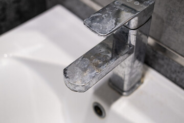 A dirty metal faucet in the sink with limescale, rust marks, and grime around the mixer, showing neglect and the need for cleaning.
