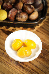 Fresh Peeled Chestnuts in Bowl with Roasted Chestnuts in Cast Iron Pan on Wooden Table