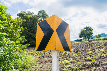 Rural landscape featuring a diagonal black arrow road sign with farmland and trees under a partly cloudy sky