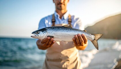Obraz premium Freshly Caught Salmon Held by a Fisherman on a Beach
