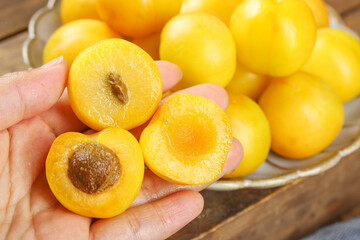 Fresh Xinjiang Apricots in Hand with Halved Fruits Showing Golden Flesh and Pits on Wooden Table