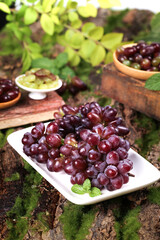 Fresh Red Grapes on White Plate with Green Leaves in Rustic Outdoor Garden Setting