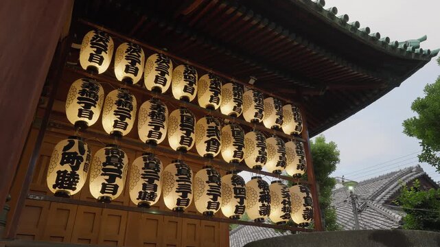 A low-angle shot of a row of illuminated, traditional Japanese lanterns hanging at a shrine gate.