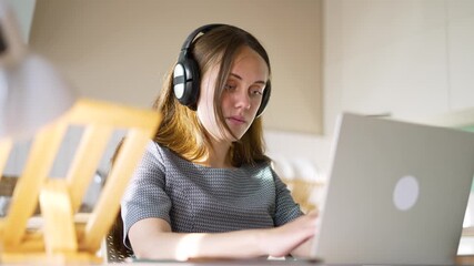 Young woman using laptop and headphone focused on study at desk in classroom student typing for online learning with concentration and calm expression while wearing headphone and looking at screen - Powered by Adobe
