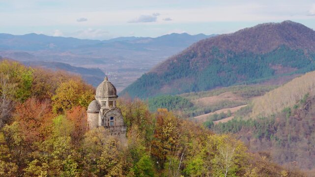 A cinematic aerial shot slowly orbits a Monumentul Eroilor in Targu Ocna, Romania, a war memorial nestled among a forest of trees in peak autumn color. The vast Romanian landscape is visible.