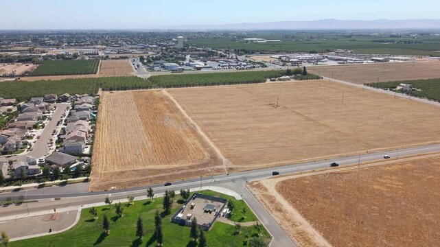 Aerial reverse shot moving from farmland and road toward sports field, with city and water tower far in background in Ripon California.