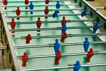 A foosball table with red and blue plastic players arranged on green field rods, ready for a game, with a shallow depth of field emphasizing the play figures