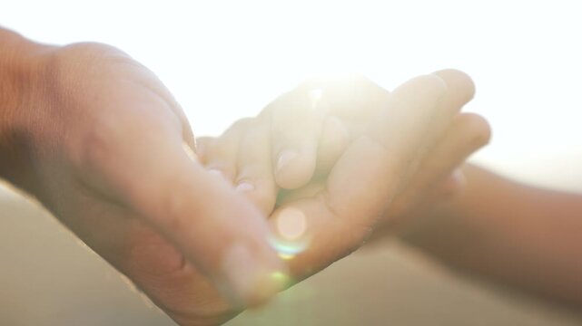 Holding baby hand in palm parent hand gently hold tiny finger with tender touch and love showing care and family bond sun flare and soft warmth emphasize tenderness and protective hold in interaction