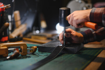Working process of the leather belt in the leather workshop. Man holding crafting tool and working